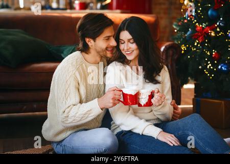 Coppia innamorata di avere il cacao natalizio accanto all'albero di Natale Foto Stock