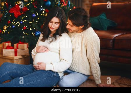 Donna incinta seduta da albero di natale con il marito Foto Stock