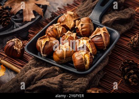 Castagne dolci arrostite commestibili in padella di ferro su un tavolo di legno Foto Stock