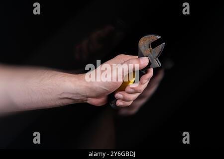 Primo piano della mano di un uomo che tiene in mano una piccola chiave da meccanico con effetto di movimento su sfondo nero Foto Stock