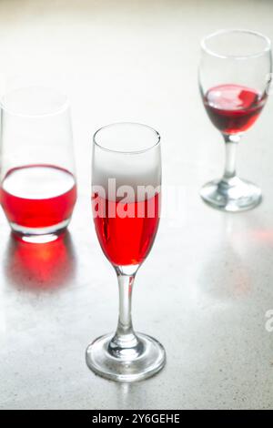 Bicchiere di champagne calice di flauto riempito con sciroppo rosso e altri tipi di bicchieri sul bancone del bar in granito sul terrazzo, vino rosso bevanda in bicchieri, parte da bere Foto Stock