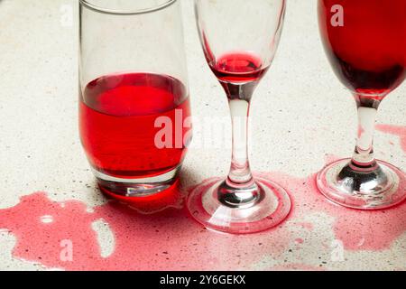 l'aspetto dell'acqua rossa di sciroppo che fuoriesce su un tavolo di granito con tre bicchieri da vino riempiti con liquido rosso Foto Stock