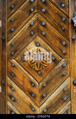 Primo piano di una porta in legno splendidamente lavorata con borchie in ferro disposte in un motivo geometrico. La ricca venatura del legno e le intagliature dettagliate riflettono la tradit Foto Stock