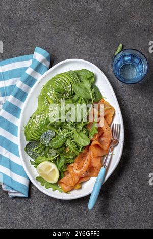 Cibo, insalata a basso contenuto di carboidrati. Insalata di spinaci, rucola con avocado e salmone. Sfondo in cemento nero, vista dall'alto Foto Stock