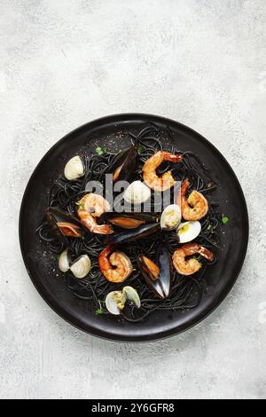 Fotografia gastronomica, spaghetti neri, con gamberi e cozze, vongole, su un piatto nero, spaghetti con gamberi, spaghetti con cozze, vista dall'alto, senza piselli Foto Stock