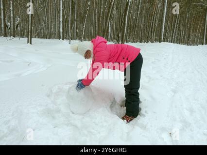 Una bambina fa un pupazzo di neve nella foresta invernale Foto Stock