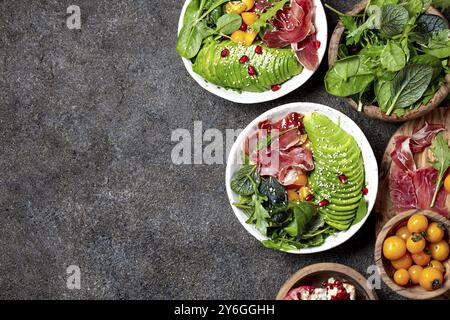 Cibo, cibo, recipiente a basso contenuto di carboidrati. Insalata fresca con spinaci verdi, rucola, avocado e prosciutto serrano in ciotola bianca, sfondo grigio, vista dall'alto Foto Stock