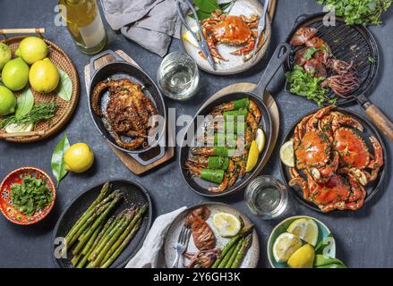 Cibo, tavolo fisso con piatti a base di pesce, granchi cotti, gamberi tigre, polpo alla griglia e calamari su piatti e padelle grigliate in ghisa, vino bianco. Vie superiori Foto Stock