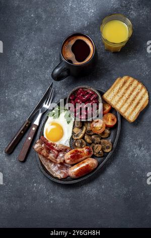 Cibo, colazione all'inglese completa con uova fritte, salsicce, pancetta, budino nero, fagioli, toast e caffè, sfondo scuro Foto Stock
