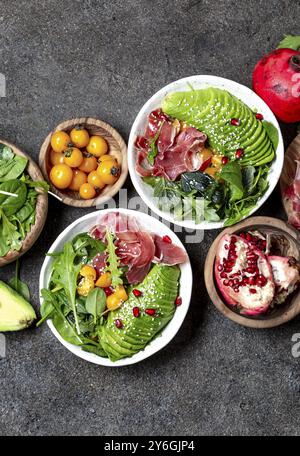 Cibo, ciotola a basso contenuto di carboidrati. Insalata fresca con spinaci verdi, rucola, avocado e prosciutto serrano in ciotola bianca, sfondo grigio, vista dall'alto Foto Stock