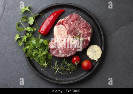 Cibo, cibo, erbe ossobuco fresche crude, aglio e pepe del cile su piatto nero. Sfondo scuro Foto Stock