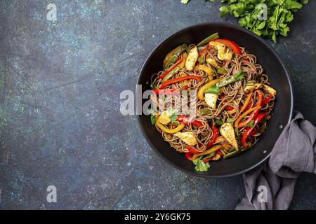 Cibo, cibo, piatto giapponese spaghetti di soba di grano saraceno con pollo e verdure carote, peperone e fagioli verdi in wok su sfondo blu scuro Foto Stock