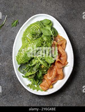 Cibo, cibo, insalata a basso contenuto di carboidrati. Insalata di spinaci, rucola con avocado e salmone. Sfondo in cemento nero, vista dall'alto Foto Stock