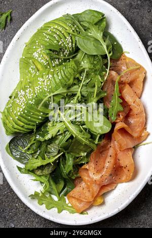 Cibo, cibo, insalata a basso contenuto di carboidrati. Insalata di spinaci, rucola con avocado e salmone. Sfondo in cemento nero, vista dall'alto Foto Stock