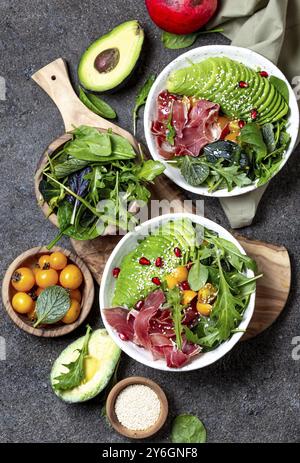 Cibo, cibo, recipiente a basso contenuto di carboidrati. Insalata fresca con spinaci verdi, rucola, avocado e prosciutto serrano in ciotola bianca, sfondo grigio, vista dall'alto Foto Stock