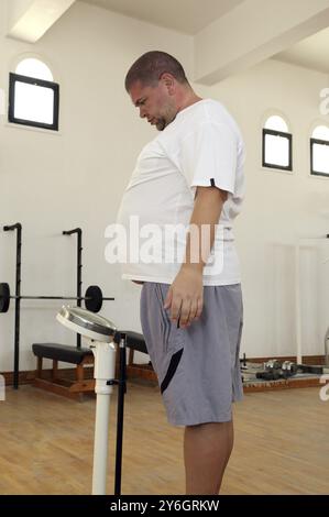 Uomo con sovrappeso in piedi su bilance in palestra Foto Stock