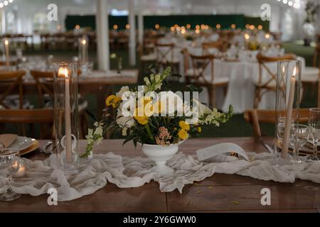 Elegante tavolo per ricevimenti nuziali con centrotavola floreale, candele e stoviglie ordinate in un ambiente splendidamente decorato. Foto Stock