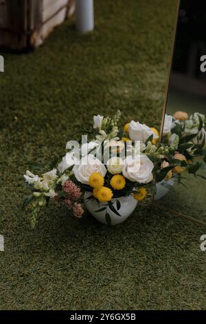 Una splendida composizione floreale con rose bianche e crisantemi gialli in un vaso bianco sull'erba. Foto Stock