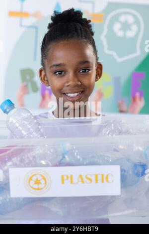 Riciclare bottiglie di plastica, una ragazza afroamericana sorridente e tenendo un contenitore in classe Foto Stock