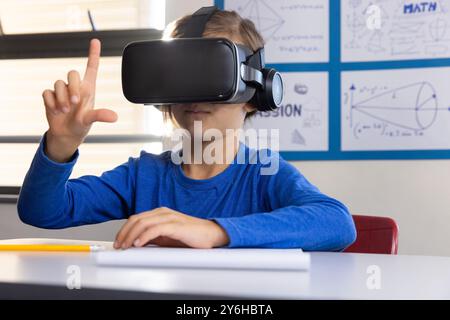 Utilizzando il visore VR, ragazzo a scuola che esplora la realtà virtuale in classe Foto Stock