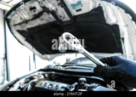 Il meccanico sta riparando un motore di un'auto , la mano del meccanico auto tiene una chiave a bussola con il vano motore di un'auto sfocato sullo sfondo , conce per la riparazione di auto Foto Stock