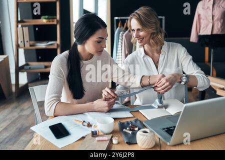 Alla ricerca di una musa alla moda. Bellissime giovani donne che lavorano sui campioni e sorridono mentre sono sedute in officina Foto Stock