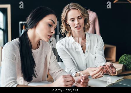 Guarda questo. Belle giovani donne che scelgono il bracciale color argento mentre sono sedute in officina Foto Stock