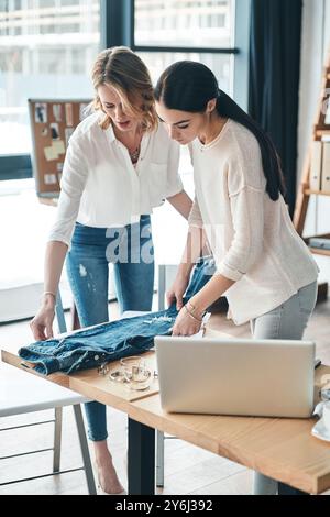 Potrebbe funzionare. Belle giovani donne che guardano i jeans e li toccano mentre passano del tempo in officina Foto Stock