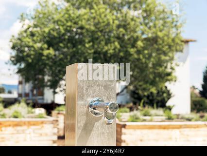 Rubinetto esterno in acciaio inox in un giardino con sfondo sfocato, che mette in risalto il concetto di ambientazione naturale Foto Stock