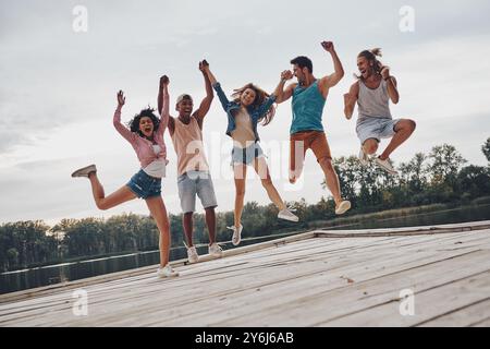 La vita è migliore con gli amici. Per tutta la lunghezza dei giovani in abbigliamento casual, sorridono e gestiscono mentre saltano sul molo Foto Stock