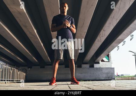 Sul serio, rimanere in forma. L'intera lunghezza di un giovane africano in abbigliamento sportivo che guarda la macchina fotografica e tiene le mani strette mentre è in piedi all'aperto Foto Stock