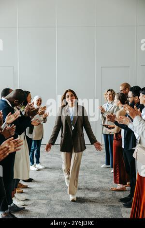 Un'auccessful leader femminile cammina tra colleghi che si sostengono applaudendo durante una riunione di lavoro in un ambiente d'ufficio moderno Foto Stock