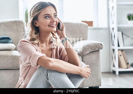 Bella chiacchierata con il fidanzato. Bella giovane donna sorridente e che parla al telefono mentre sta pavimentando a casa Foto Stock