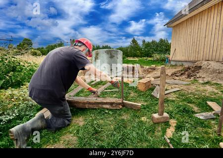 Il lavoratore abbassa l'anello di calcestruzzo nella fossa utilizzando un verricello manuale durante la costruzione del serbatoio settico. Foto Stock