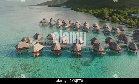 Lussuosi bungalow sull'acqua con tetti di paglia in fila sulle acque turchesi della laguna dell'isola di Moorea nella Polinesia francese. Vacanza esotica, romantica luna di miele. Ripresa aerea Foto Stock