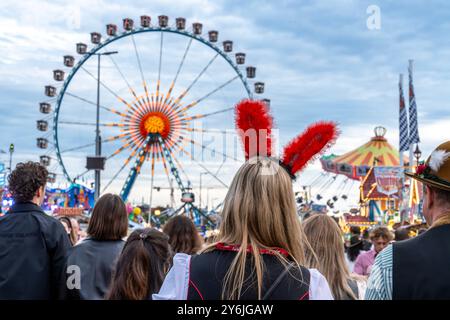 Wiesnbummel, viele Münchner und Touristen sind am frühen Mittwochabend auf dem Oktoberfest unterwegs, München, settembre 2024 Deutschland, München, settembre 2024, Wiesnbesucher bummeln über die Festwiese, Frau mit dekorativem Haarreif mit roten Puschelohren, Fahrgeschäfte Riesenrad und Karussell, Himmel bedeckt, Wiesnwetter verschlechtert sich, bayerisch, Oktoberfest 2024, Volksfest, Bayern, *** Wiesnbummel, molti residenti di Monaco e turisti sono fuori e intorno all'Oktoberfest inizio mercoledì sera, Monaco, settembre 2024 Germania, Monaco, settembre 2024, i visitatori di Wiesn passeggiano lungo la strada Foto Stock