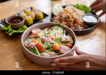 Primo piano di una cameriera che serve cibo a un tavolo in un ristorante, con una deliziosa insalata salutare, riso fritto e gnocchi. Foto Stock