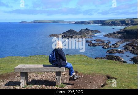 Donna solitaria seduta su una panchina di legno presso il Path a Park Head vicino a Porthcothan sul Southwest Coastal Path, North Cornwall, Inghilterra, Regno Unito. Foto Stock