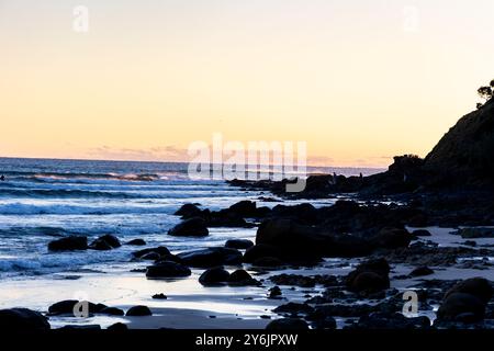 Una vista panoramica di una spiaggia rocciosa al tramonto con le onde dell'oceano che si infrangono dolcemente sulla riva. Foto Stock