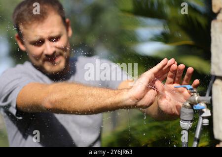 Uomo che evita di bagnarsi con una perdita di rubinetto nel giardino di casa Foto Stock