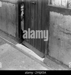 Case prefabbricate del dopoguerra , Inghilterra fine anni '1940 Un bambino che guarda fuori da dietro una porta. Foto Stock