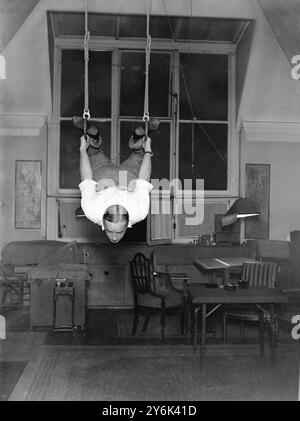 Edmund Dulac , il celebre artista del suo studio 117 Ladbrooke Road . Il signor Dulac credeva nella necessità di mantenersi in forma e di fare esercizi quotidiani su anelli da palestra sospesi dal soffitto del suo studio. 10 ottobre 1929 Foto Stock
