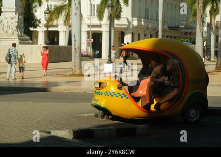 L'Avana, Cuba 2024 aprile. I tassisti passano in taxi giallo coco, al Parque Central, in attesa di passeggeri. Turisti che scattano foto in background Foto Stock