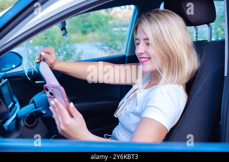 Sorridente giovane donna che usa un'app sul suo smartphone all'interno di un'auto Foto Stock