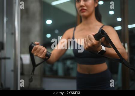 Giovane donna in forma con abbigliamento sportivo che solleva pesi utilizzando una macchina via cavo in palestra Foto Stock