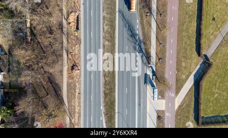 Vista aerea di un'auto che guida su una strada divisa con una mediana erbosa, circondata da alberi e sentieri Foto Stock