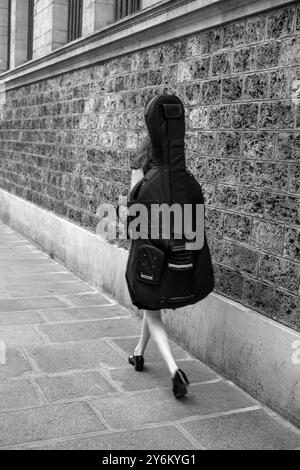 Francia, Parigi, 5° arrondissement, Rue Clovis, giovane donna che cammina con il violoncello sulla schiena, giugno 2022. Foto Stock