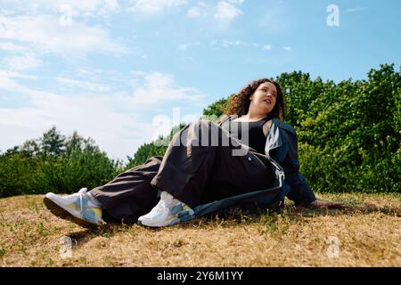 Una donna gioiosa si rilassa in un campo illuminato dal sole, circondato da vegetazione lussureggiante e cieli limpidi. Foto Stock