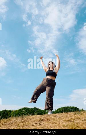Una donna allegra e grande balla liberamente in un campo vivace sotto un cielo blu brillante. Foto Stock