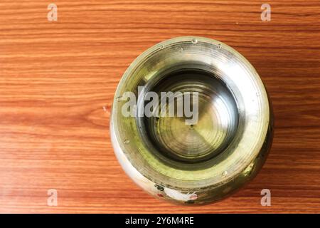 Vaso in acciaio in ottone "Kalash" (lota), un tradizionale contenitore d'acqua globulare, posto su uno sfondo marrone legno, che mette in risalto la sua cultura e utilità Foto Stock